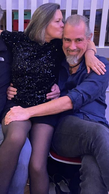Eine Frau sitzt auf dem Schoß eines Mannes, beide lächeln und scheinen fröhlich zu sein.