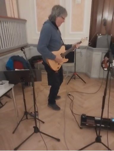 Musiker spielt E-Gitarre in einem Saal mit Stativ und Notenständern.