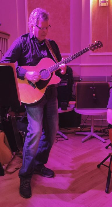 Mann spielt Akustikgitarre in gedämpfter Beleuchtung.