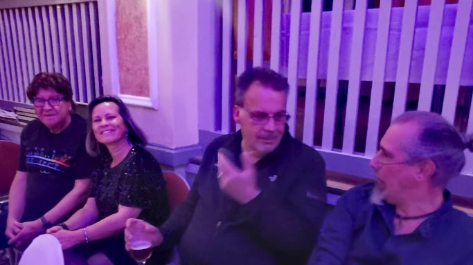 Vier Personen sitzen in einer Reihe in einem Raum mit buntem Licht.